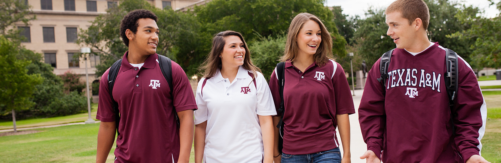 a group of four ethnically diverse TAMU students walking in front of the administration building